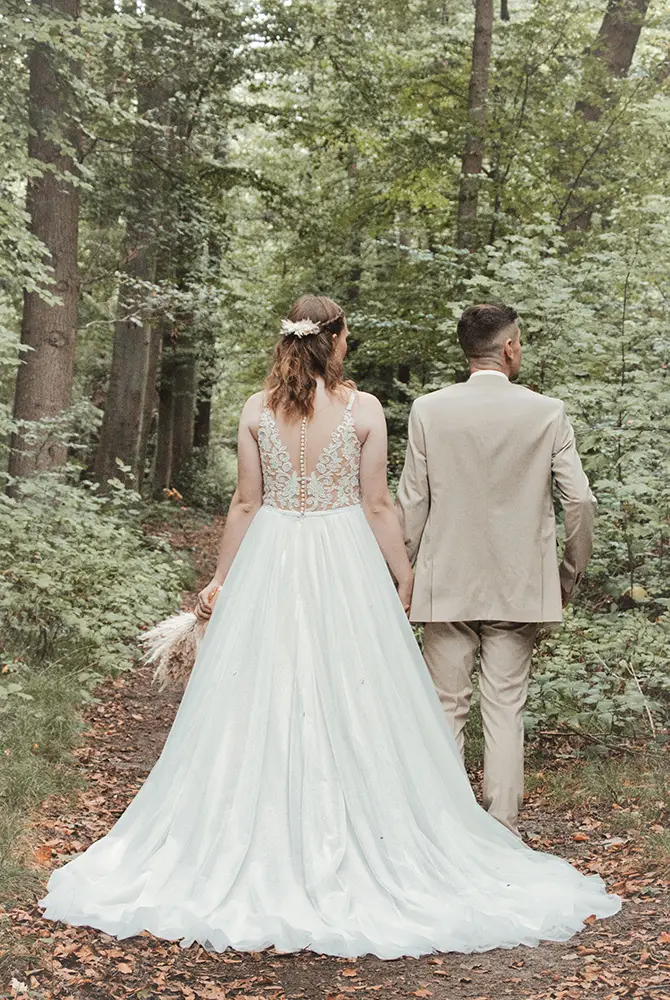 Brautpaar steht im Wald und wurde von hinten fotografiert